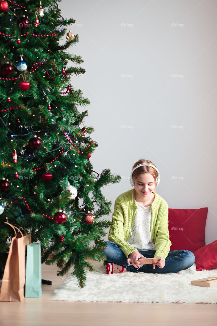 Teenage girl listening music in front christmas tree
