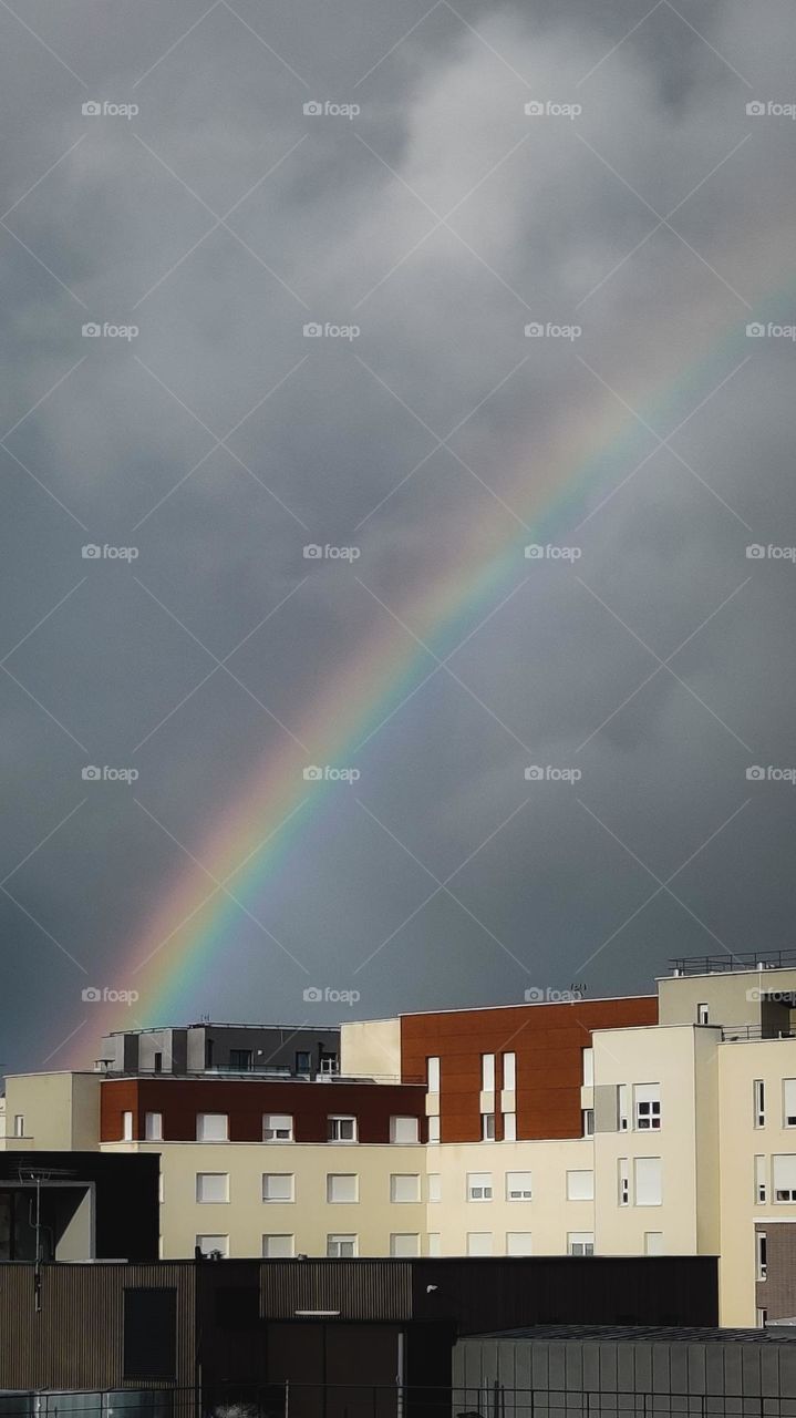 Rainbow across gray skies with residences in foreground.