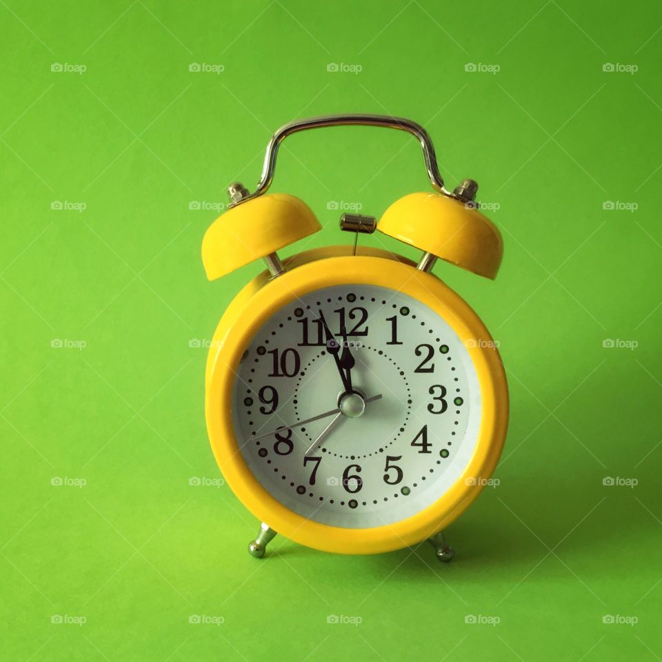 Yellow alarm clock on green background