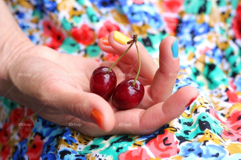 A hand holds cherry fruit on colorful background