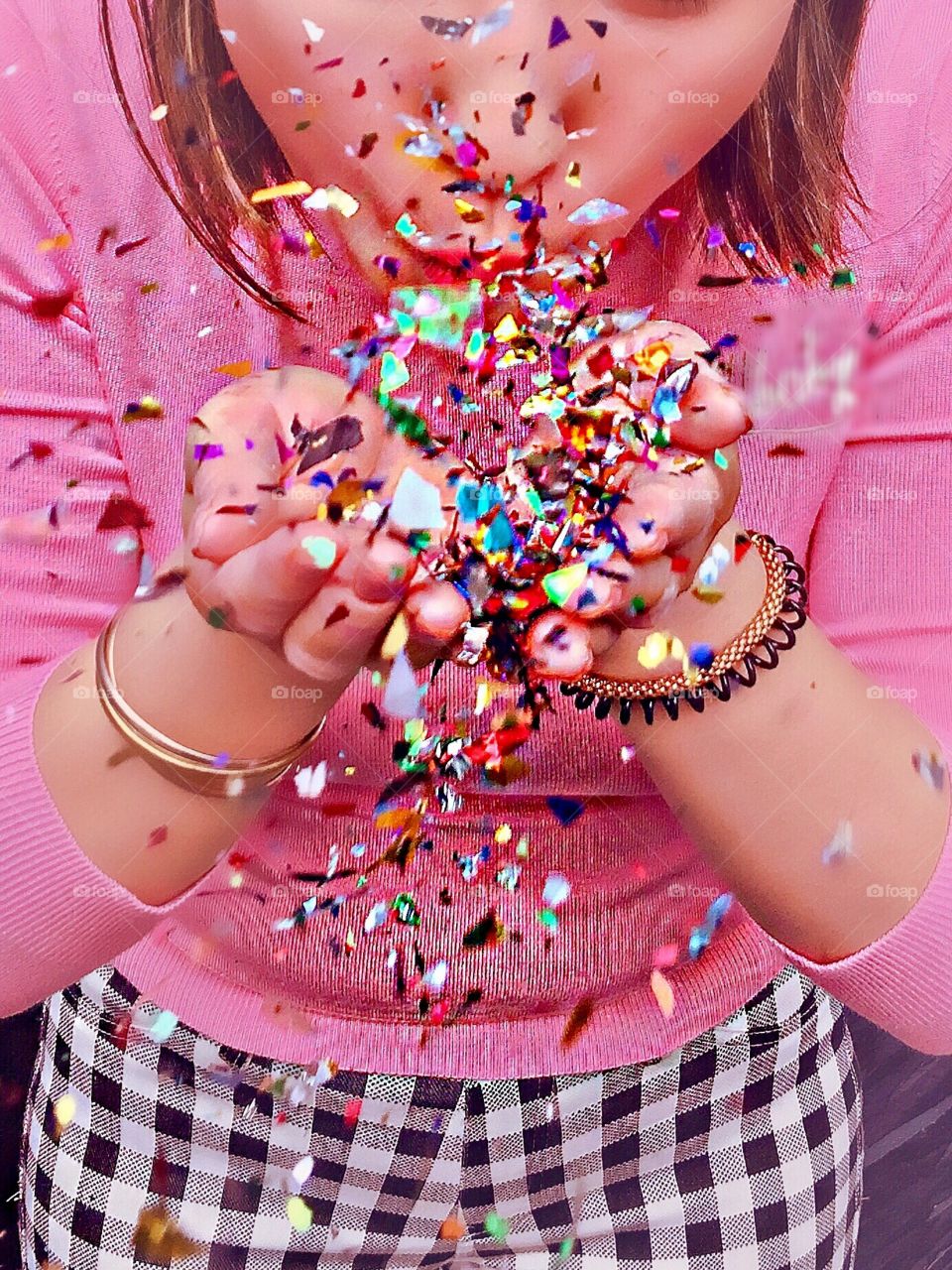 Girl in pink standing against a pink wall, blowing glitter confetti. 