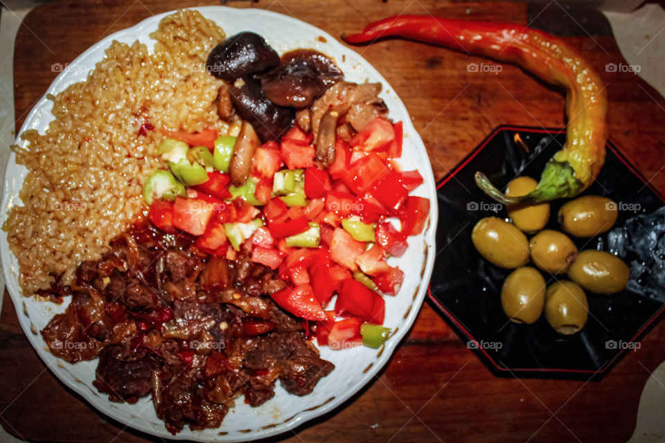 Served on a plate: chopped beef prepared in soy sauce, tomato chopped with chopped green peppers, rice with soy sauce; second tanner: large green olives; garnish green red pepper