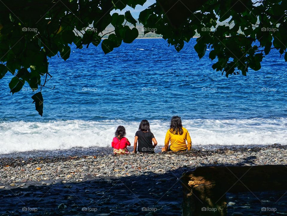 Three kids sit down together in beach