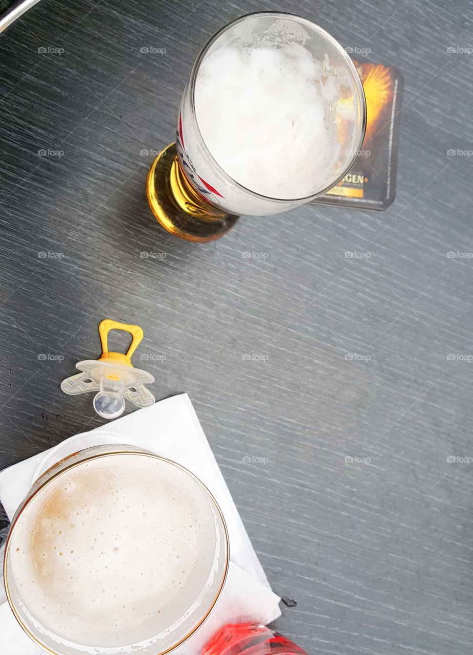 Yellow baby pacifier on a black cafe terrace table with two glasses of blonde beer for happy hour with parents and child
