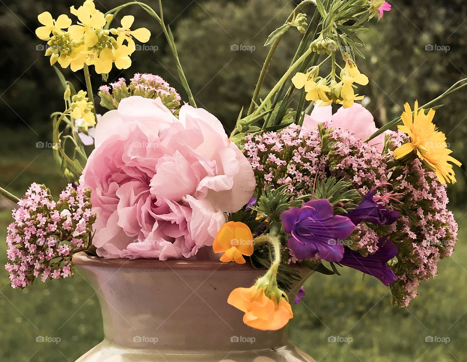 Tightly cropped image of springtime wildflowers in a vase, with foliage seen in the background 