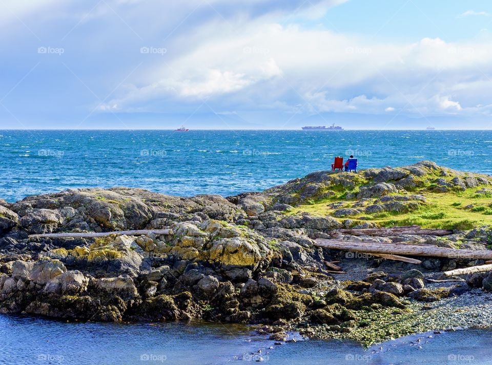 Two people in warm hats sitting under clouds on scenic ocean island 