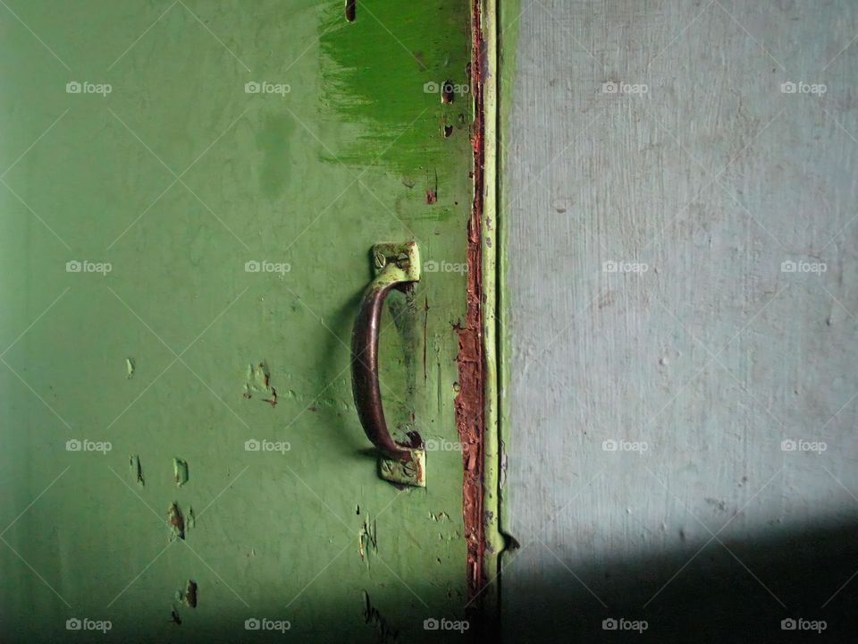 Close-up of a dark green door with an iron handle for opening