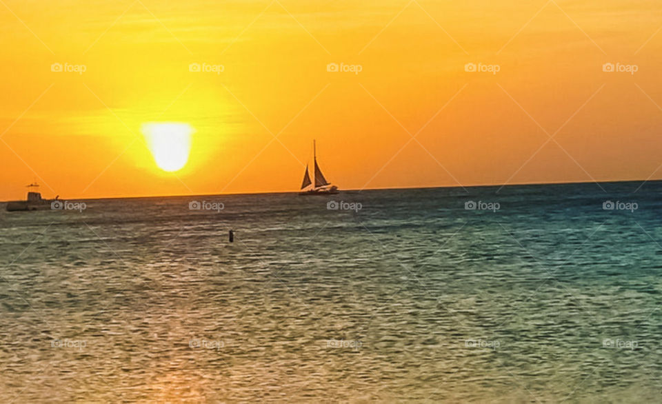 Orange Sky sunset in Aruba. View of ocean ripples and sailboat in the distance.