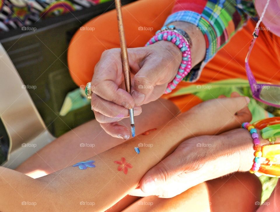 Old woman painting flowers on a child's arm at a festival