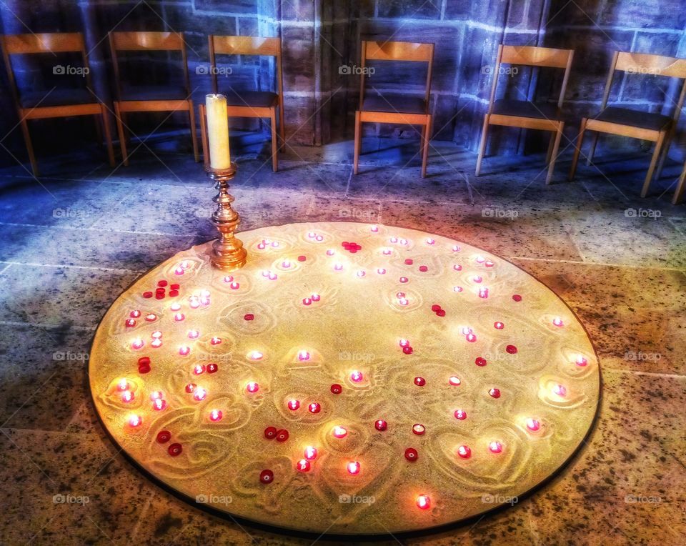 Candles in a circle of sand shining brightly. They share warmth, thoughts and love of people who lit them