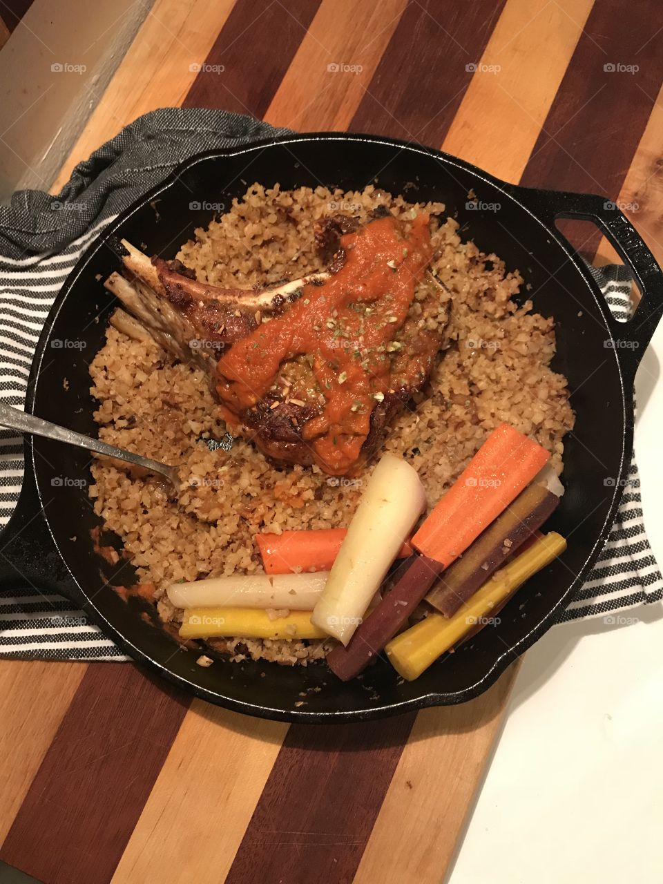 Extra thick pork chop on a bed of riced cauliflower with friends colored carrots and butternut squash and carrot purée in an iron skillet 