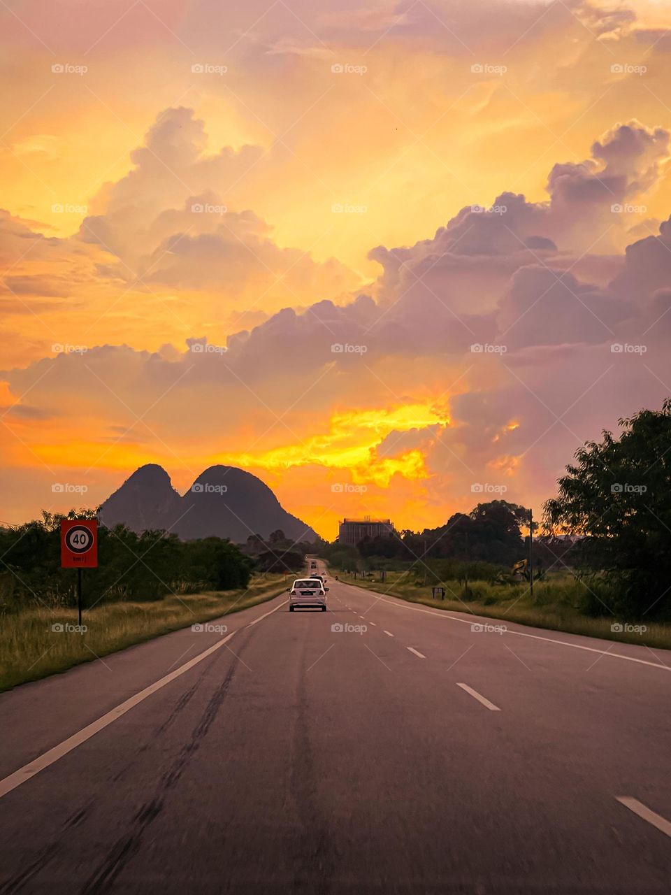 Beautiful view of the sunset and long road trip journey. Hills and pinkish and orange clouds as the background 