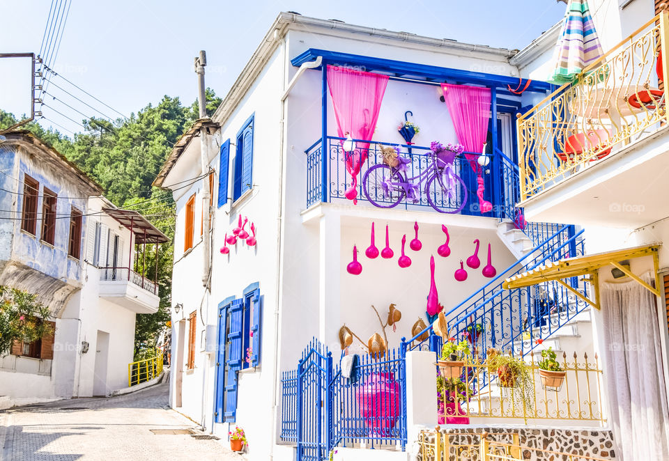 Greek Traditional House With Blue Windows , White Wall, Flowers And Pink Decorative Pumpkins
