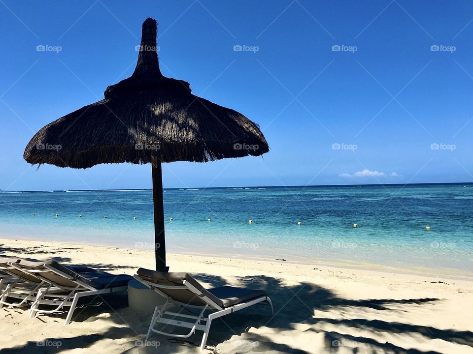 Sunshine and blue skies at the beach. Relaxing scene on Mauritius coast with sun loungers and umbrella