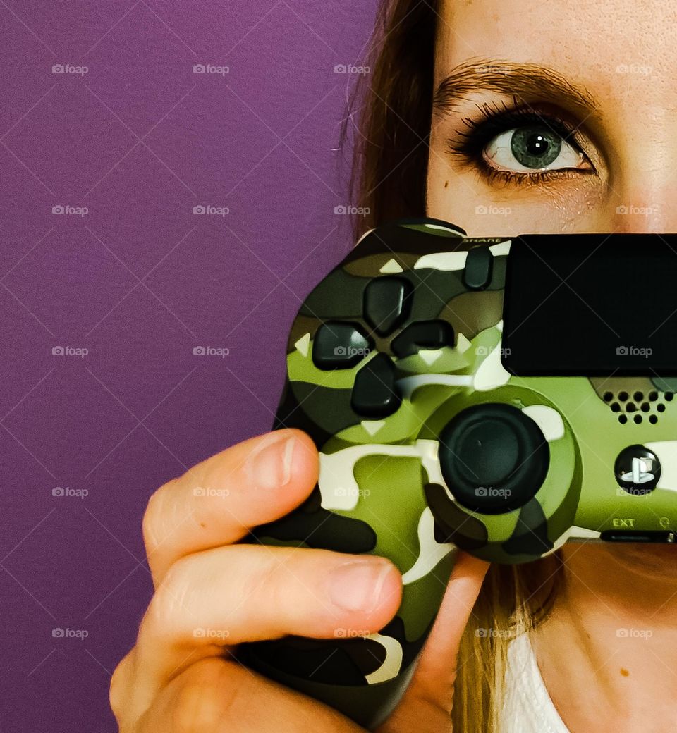 Pretty girl gamer facing camera holding up her camo Playstation 4 game controller