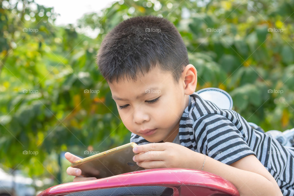 Portrait of Asian boys are playing mobile phones in park.