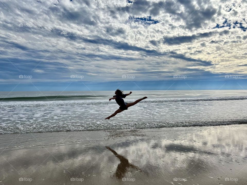 A gymnast dances in the surf on a beach with clouds and waves. 
