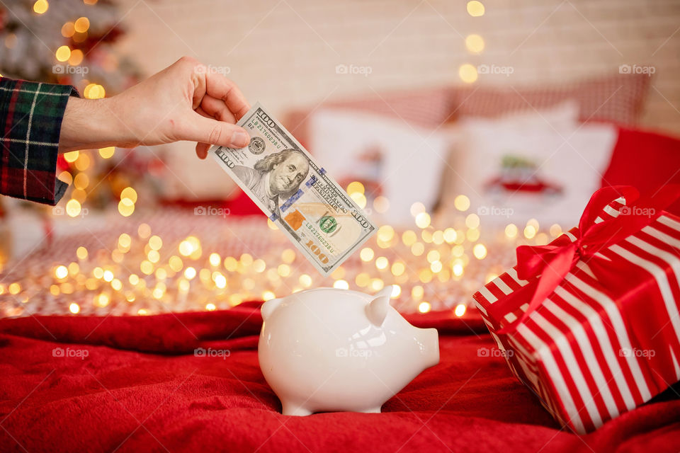 piggy bank with 100 dollars banknote in festive New Year atmosphere of scenery. Magical bokeh with Christmas tree and bright lights.