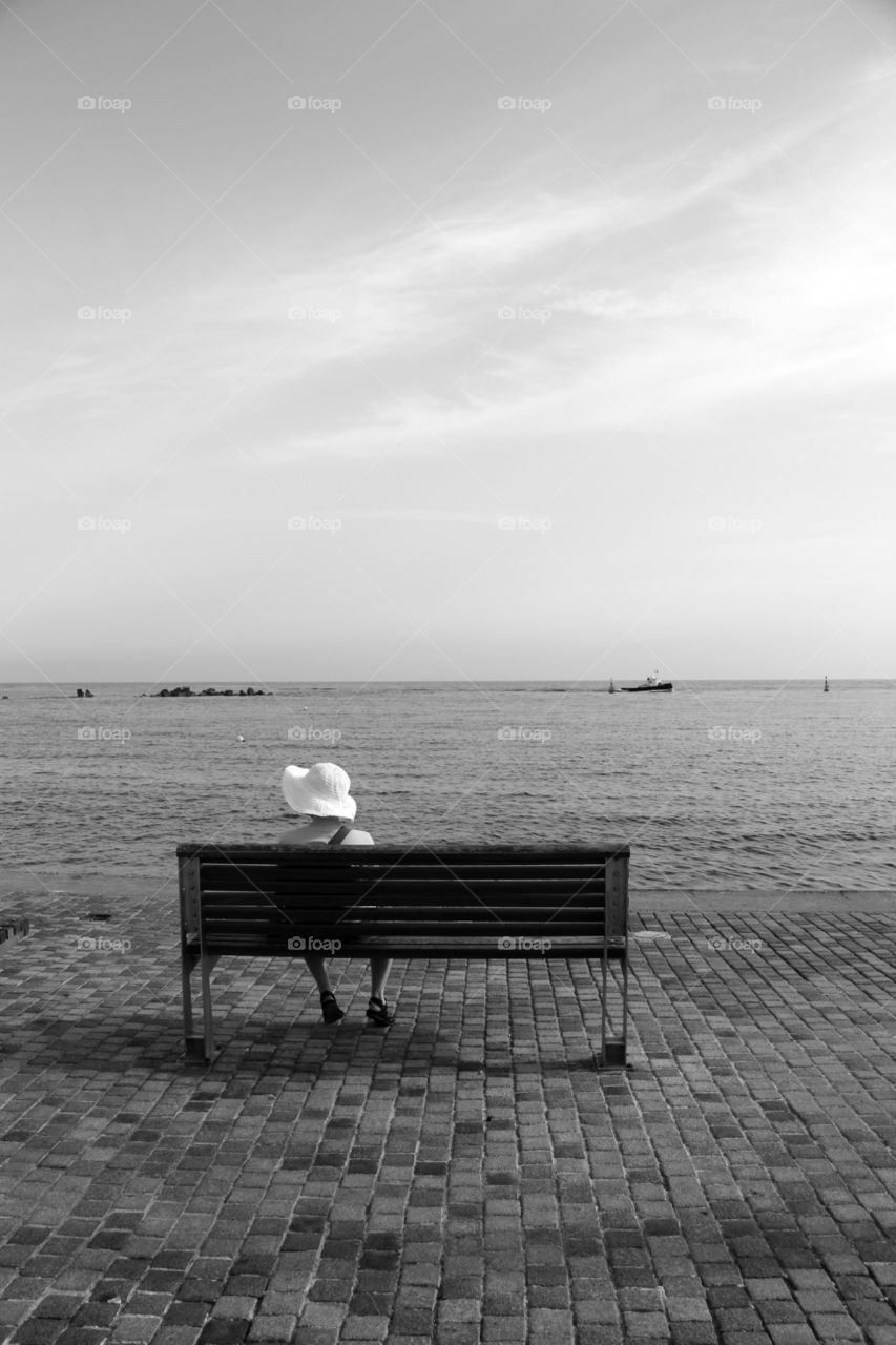A lady all alone sat on a wooden bench looking out to sea