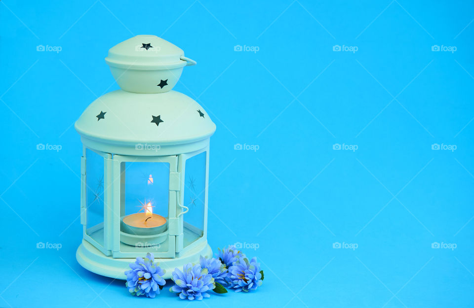 Lanterns with candle light and flowers on blue background with copy space 