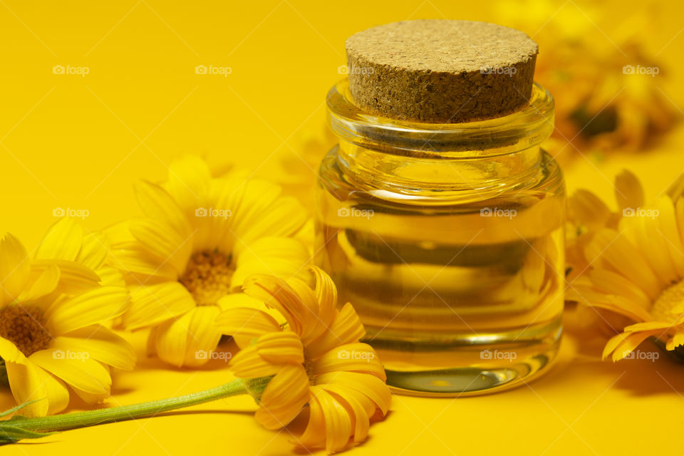 Calendula products. Essential oil . Small bottle of calendula oil (Pot marigold extract, tincture, infusion) . aromatherapy essential oil with fresh marigold flowers on yellow background. Naturopathic