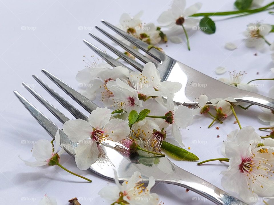 Close up of two metal forks decorated with white flowers on the white table