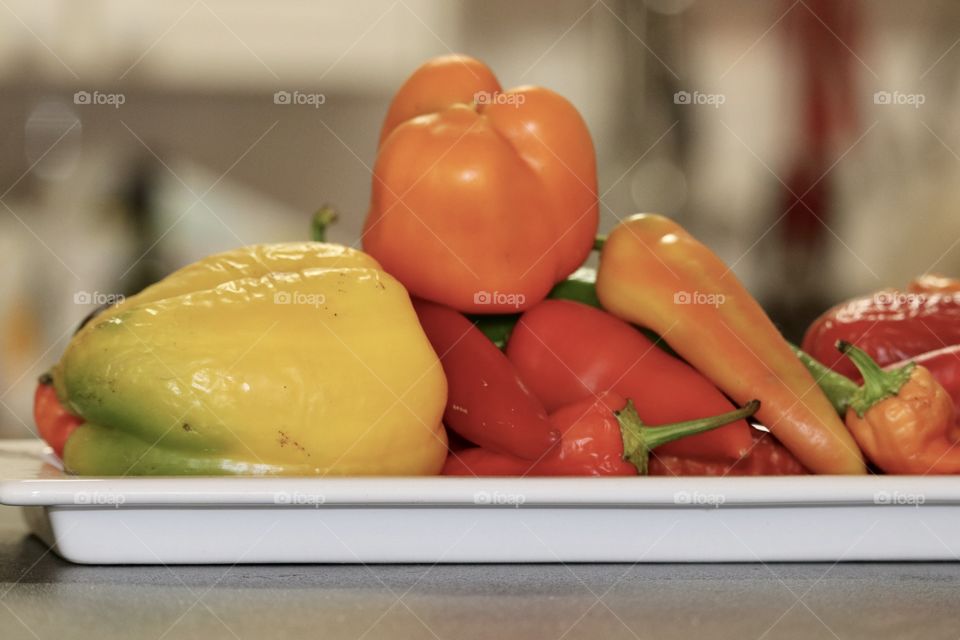 Orange sweet bell pepper atop mound of multi coloured sweet bell peppers still life