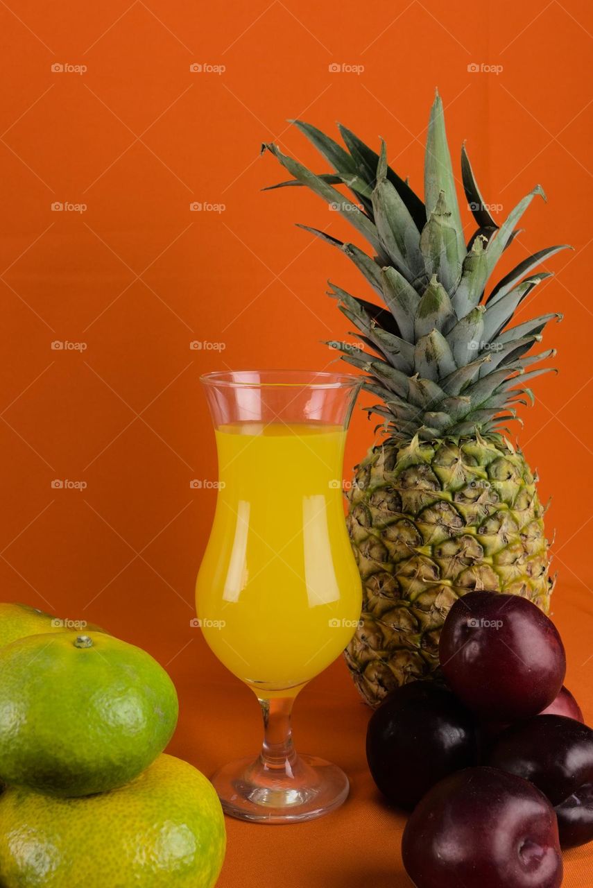 Red plums and crystal glass with natural juice on orange colored background