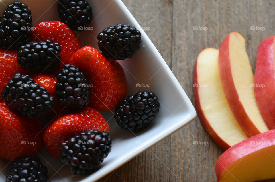 Bowl of strawberries and blackberries with apple slices on a wood background