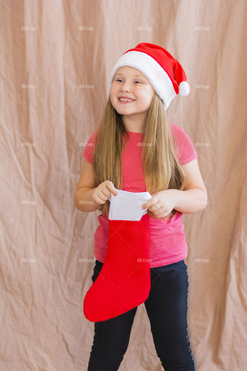 Happy smiling girl 6 years old wearing a santa claus hat with a Christmas red boot wave of the hand copy space  