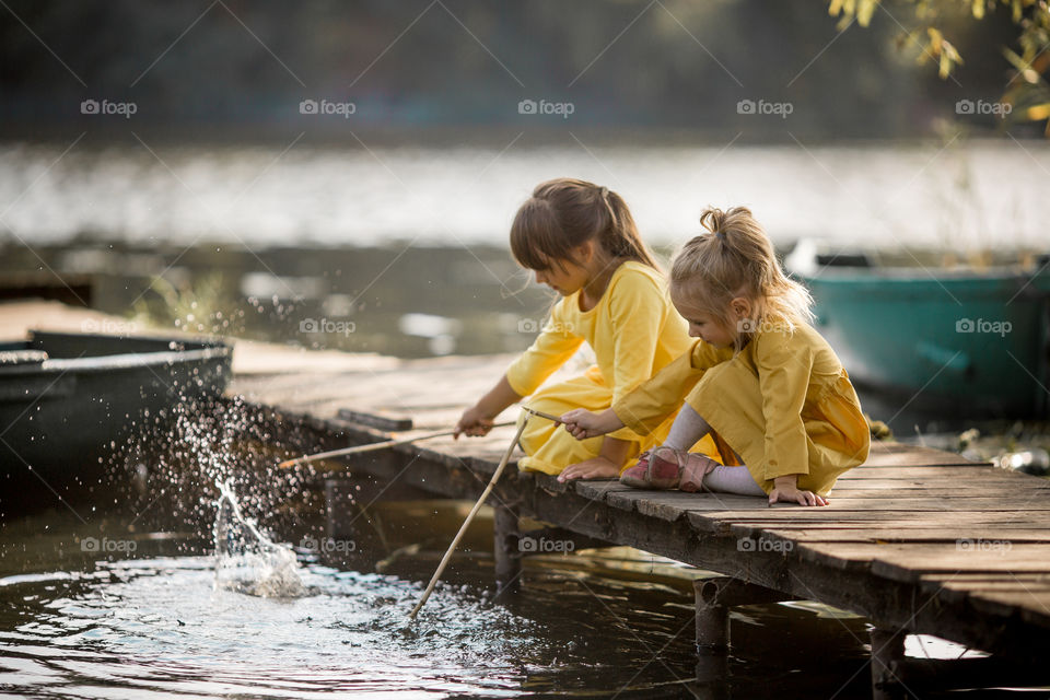 Little sisters playing near lake at autumn day 