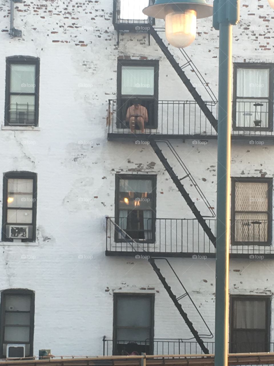 Man sitting on fire escape on computer during a hot summer day 