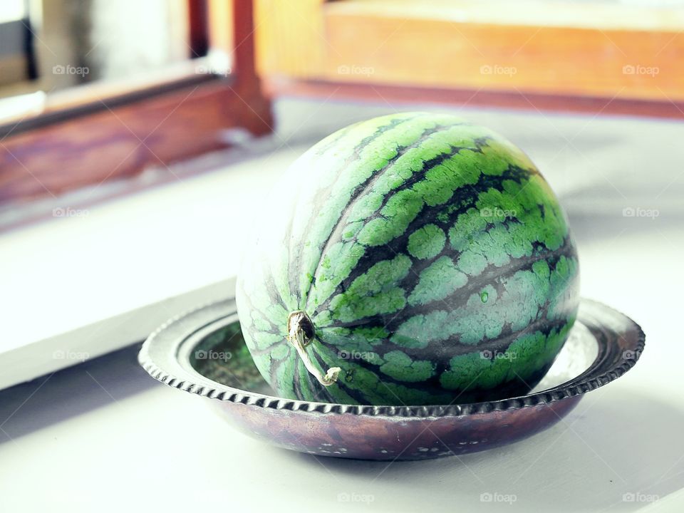 Watermelon in a metal plate on the windowsill 