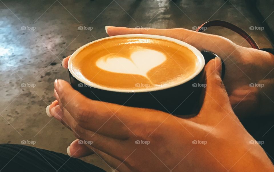 A hot cup of coffee warms the hand , Cute white heart from milk foam 