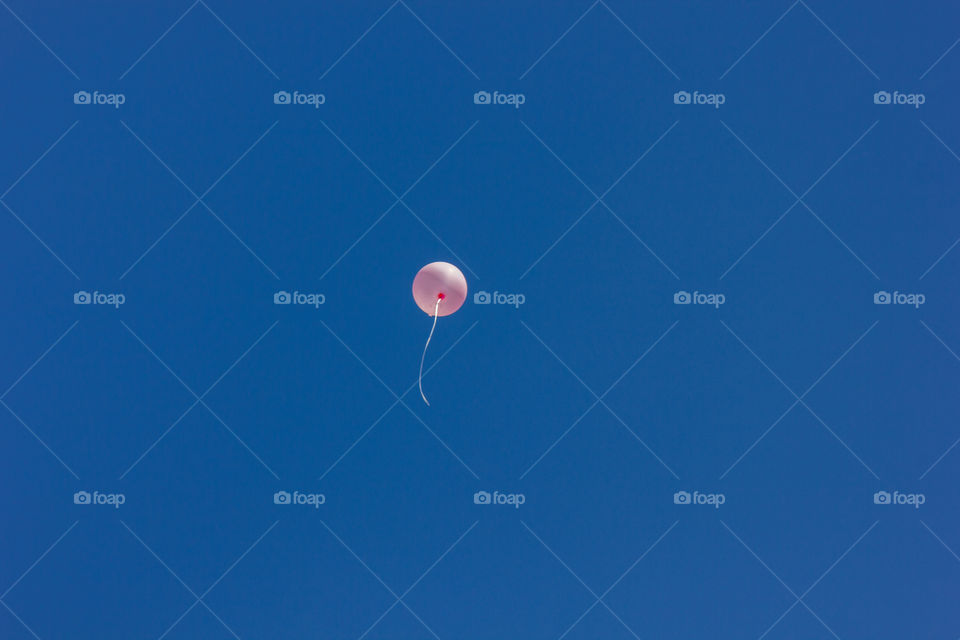 One single pink balloon in the blue sky