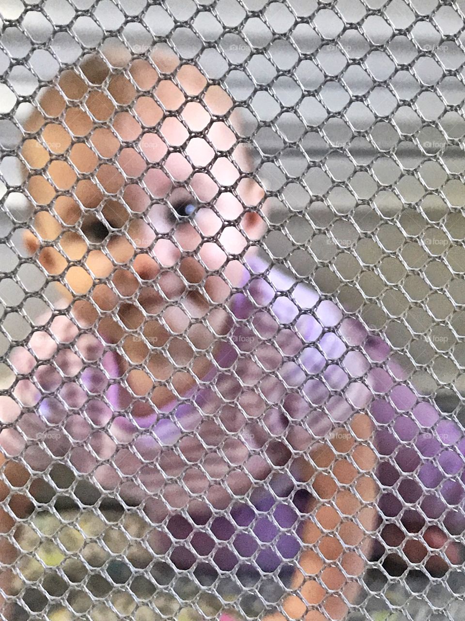 A baby looking through the textures and patterns of a playpen.