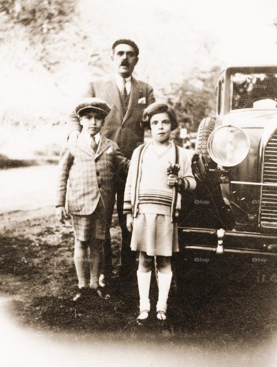 Sepia vintage shot of a man, his daughter and his son posing by his car in the countryside in1930
