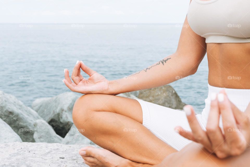 Crop photo of young fit beautiful woman with long hair in white sport clothes practice yoga and enjoy life on the sea beach, mental and phisical health