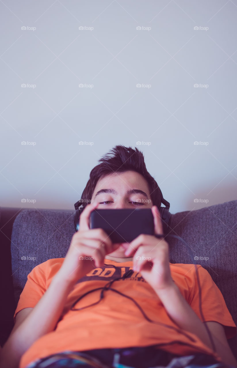 Teenage boy lying on sofa with headphones and mobile phone