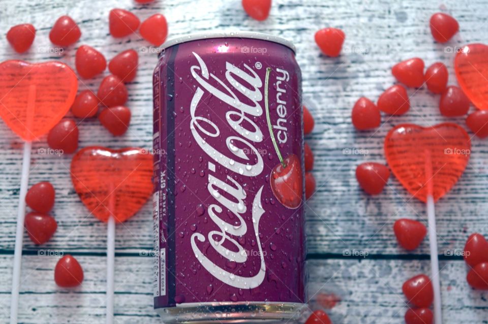 A can of cherry Coca-Cola with candy hearts and a white rustic background