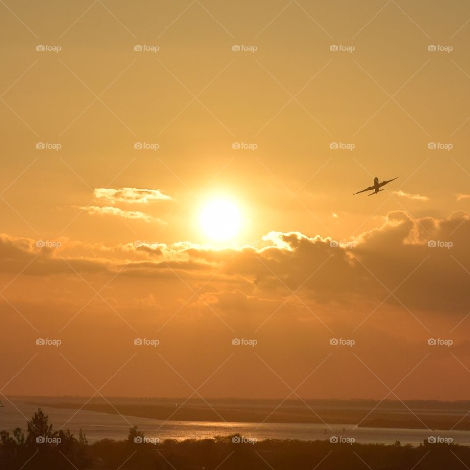 An airplane flying through the beautiful orange sunset sky in Hawaii