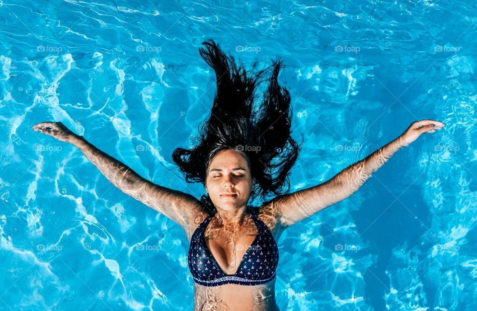 Overhead photo of young woman wearing blue bikini, relaxing and floating in swimming pool