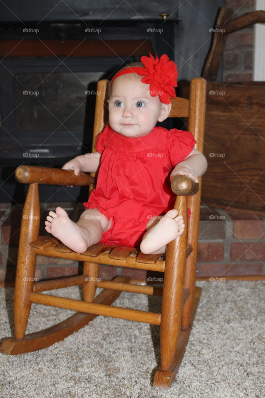 Baby girl in red dress sitting in rocking chair