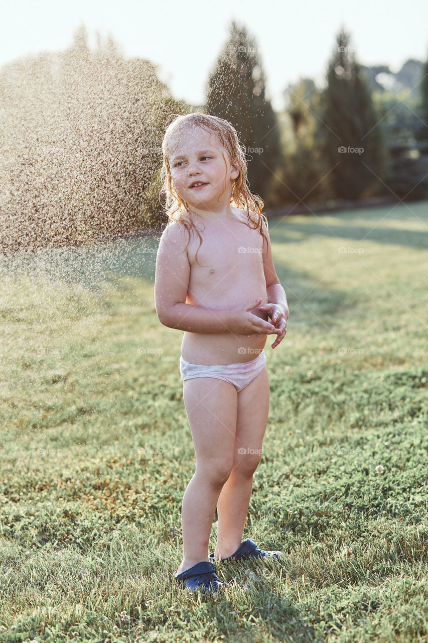 Little cute adorable girl enjoying a cool water sprayed by her father during hot summer day in backyard. Candid people, real moments, authentic situations