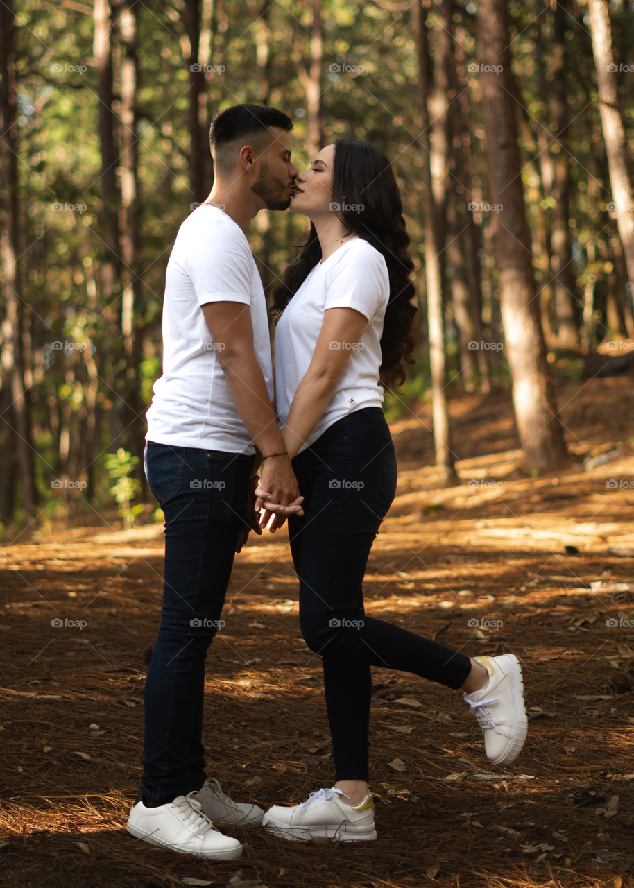 Couples of young people sitting in middle of the forest while looking into their eyes and kissing, in a sunny day.