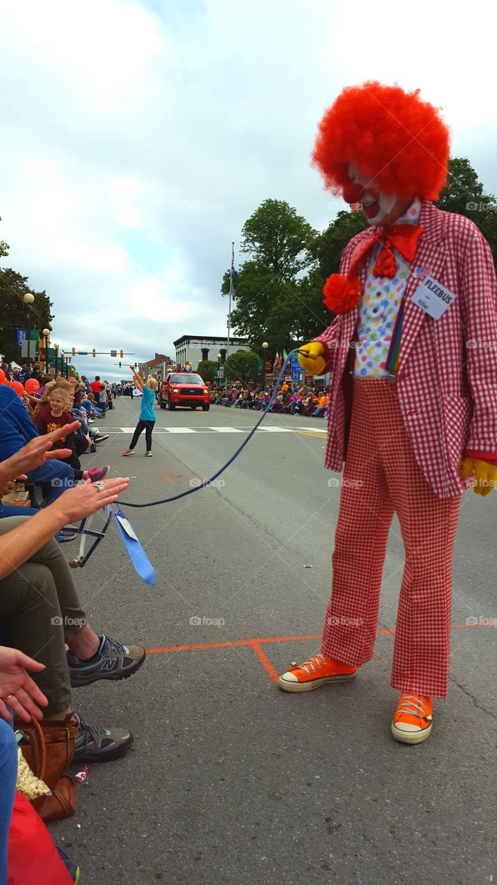 A clown and his invisible dog walk the streets during a hometown parade.