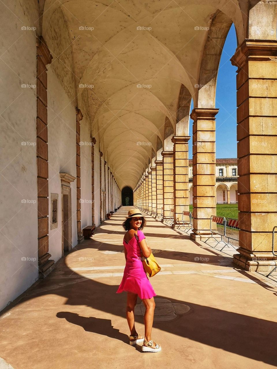 smiling woman in fuchsia dress under the colonnade of an ancient palace