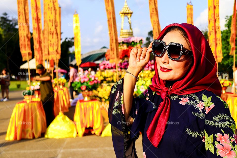 Portrait of a beautiful mother wearing a red hijab, wearing a floral patterned robe and wearing black glasses, taking a photo with a happy expression.