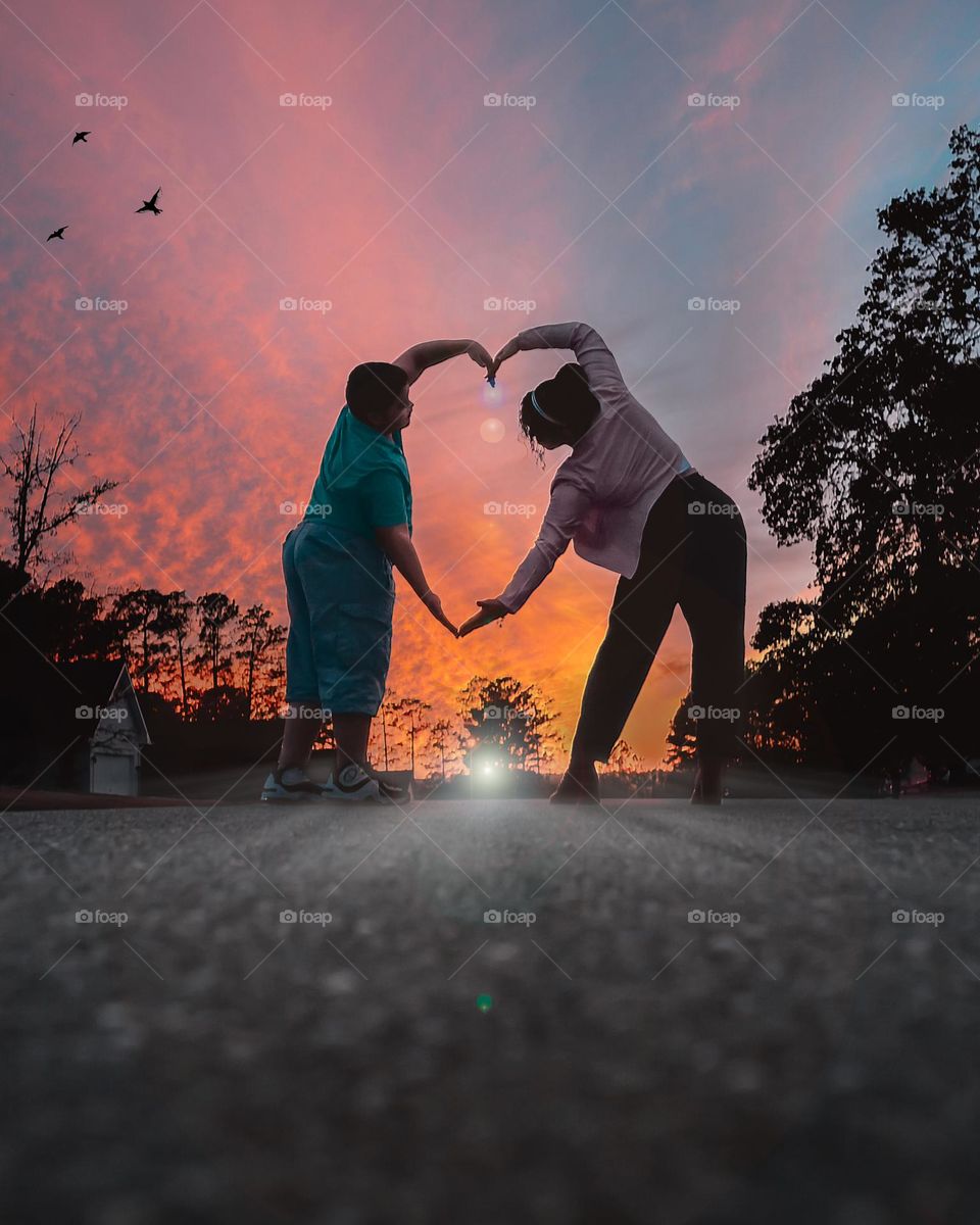 Mother and son making a heartwarming gesture creating a heart with our hands against the beautiful sunset 