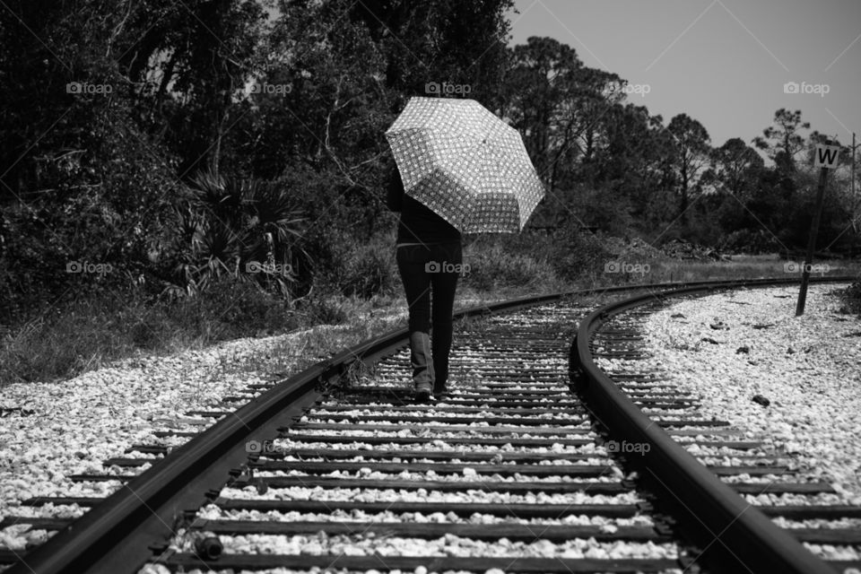 Walking upon lonely railroad tracks with umbrella onto the unknown